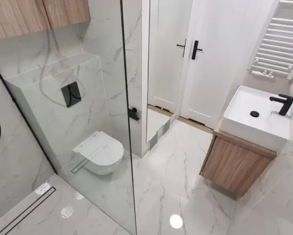 Nowoczesna łazienka z prysznicem walk-in, umywalką nablatową i podwieszaną toaletą. Eleganckie płytki imitujące marmur i drewniane akcenty. Remont łazienki koszt może być różny, ale efekt jest wart inwestycji.