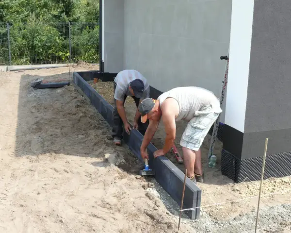 Dwóch mężczyzn układa obrzeża. Prawidłowe suchy beton proporcje są kluczowe dla trwałości.
