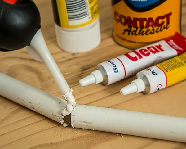 Aplikacja kleju butapren na pękniętą białą rurkę. W tle tubki z klejem i puszka "Contact Adhesive".