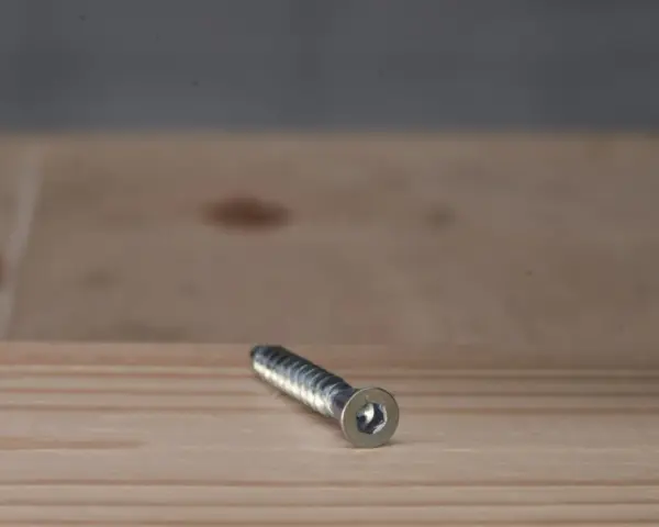 Metalowy konfirmat z gniazdem sześciokątnym leży na drewnianej powierzchni.