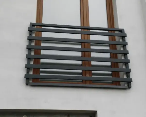 Nowoczesne balkony francuskie z ciemnoszarymi, poziomymi barierkami na tle białej ściany i brązowych okien.