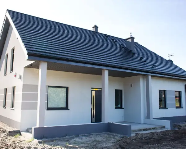 Nowy dom z szarą dachówką i jasną elewacją, gotowy do malowania. Eleganckie wykończenie podkreśla nowoczesny styl.