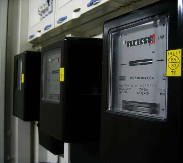 Rząd czarnych liczników energii elektrycznej. Na pierwszym liczniku widoczny odczyt 3104577 kWh.