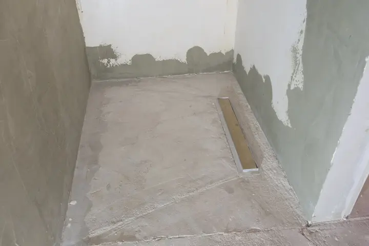 Niedawno położony szlam mineralny w łazience, z widocznym odpływem liniowym. Ściany w trakcie tynkowania.