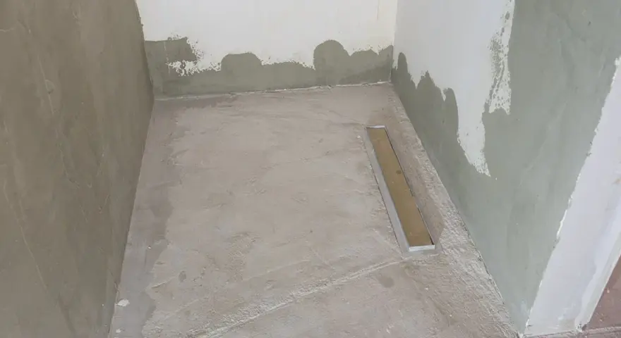 Niedawno położony szlam mineralny w łazience, z widocznym odpływem liniowym. Ściany w trakcie tynkowania.
