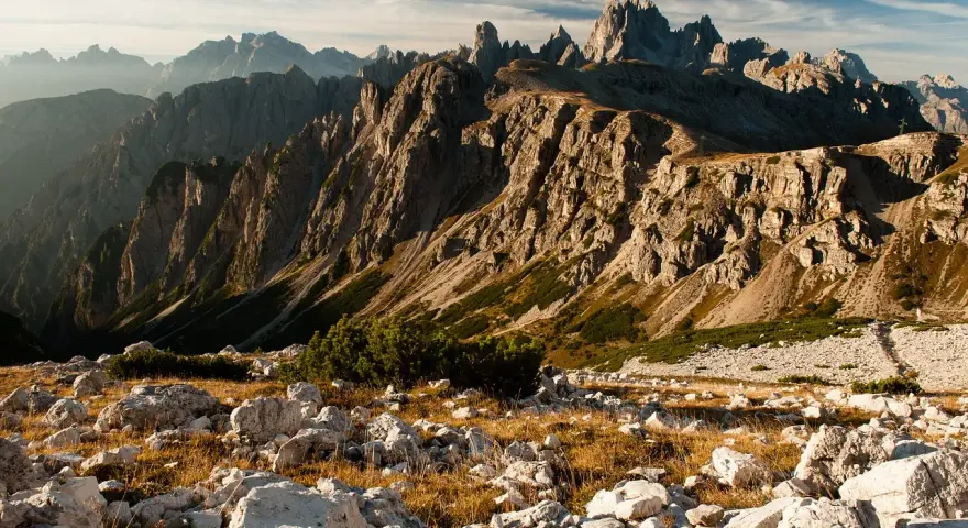 Skaliste szczyty Dolomitów o wschodzie słońca, z kamienistym zboczem i suchą trawą na pierwszym planie.