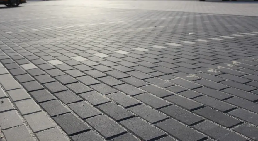 Szary parking wyłożony kostką brukową holland. W tle widać zaparkowane samochody.