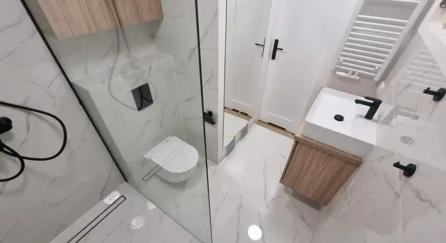 Nowoczesna łazienka z prysznicem walk-in, umywalką nablatową i podwieszaną toaletą. Eleganckie płytki imitujące marmur i drewniane akcenty. Remont łazienki koszt może być różny, ale efekt jest wart inwestycji.