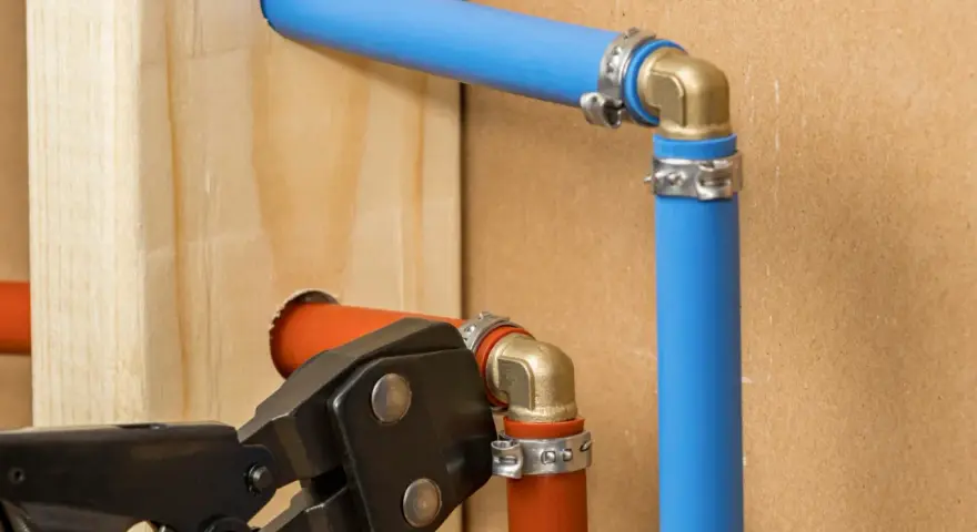 Instalacja hydrauliczna z rurami pex. Narzędzie do zaciskania łączy pomarańczową rurę z mosiężnym kolankiem.