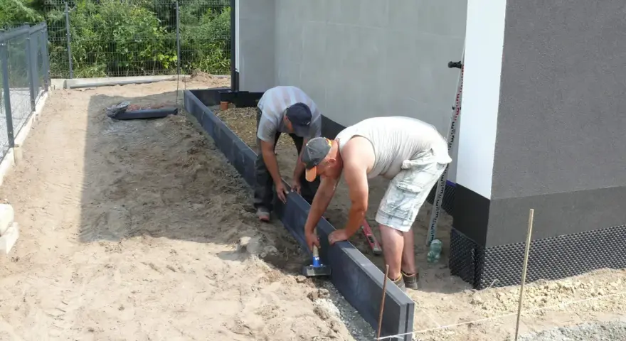 Dwóch mężczyzn układa obrzeża. Prawidłowe suchy beton proporcje są kluczowe dla trwałości.