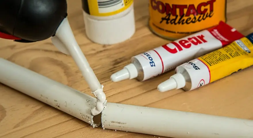 Aplikacja kleju butapren na pękniętą białą rurkę. W tle tubki z klejem i puszka "Contact Adhesive".