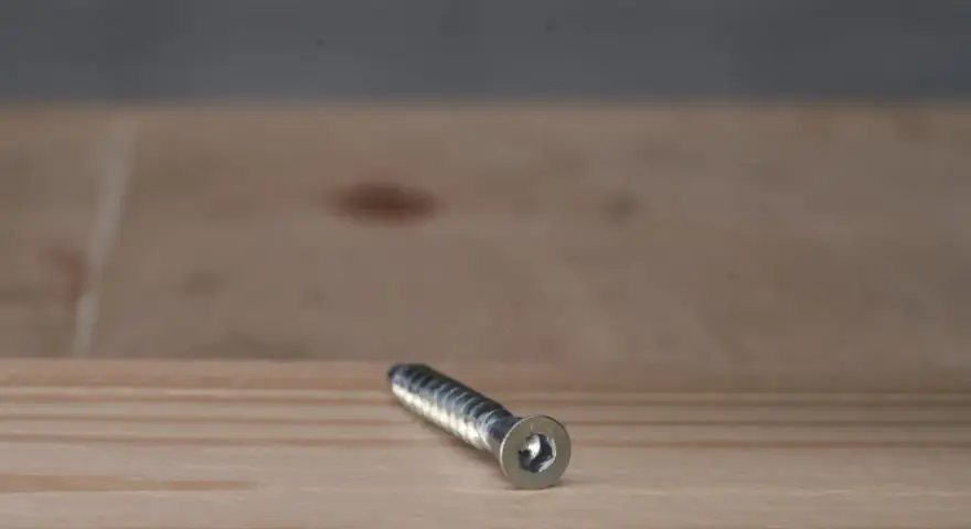 Metalowy konfirmat z gniazdem sześciokątnym leży na drewnianej powierzchni.