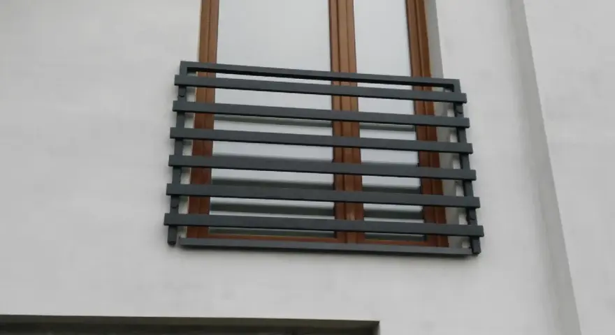 Nowoczesne balkony francuskie z ciemnoszarymi, poziomymi barierkami na tle białej ściany i brązowych okien.