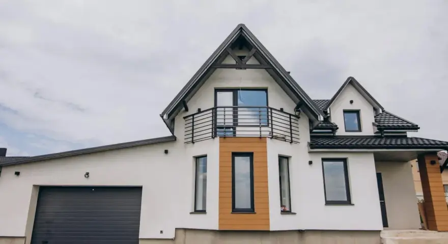 Nowoczesny dom z garażem i balkonem. Elegancki gzyms podkreśla architekturę budynku, a drewniane elementy dodają ciepła.