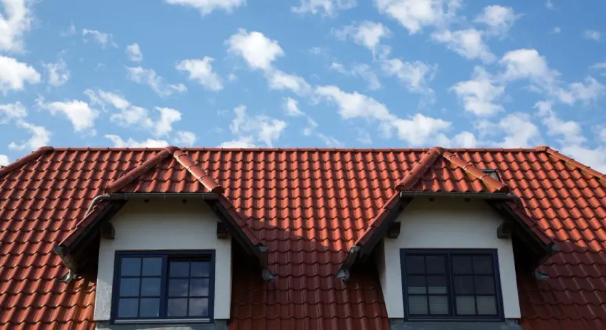Dachówka ceramiczna w kolorze ceglastym pokrywa dach domu z dwoma lukarnami. Różne rodzaje dachówek tworzą harmonijną całość.