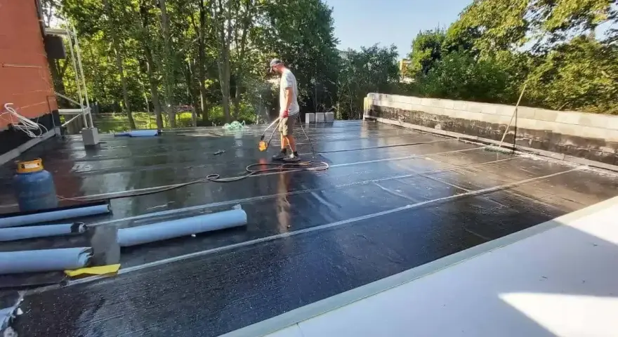 Pracownik wykonuje hydroizolację tarasu nad garażem, używając palnika do papy.