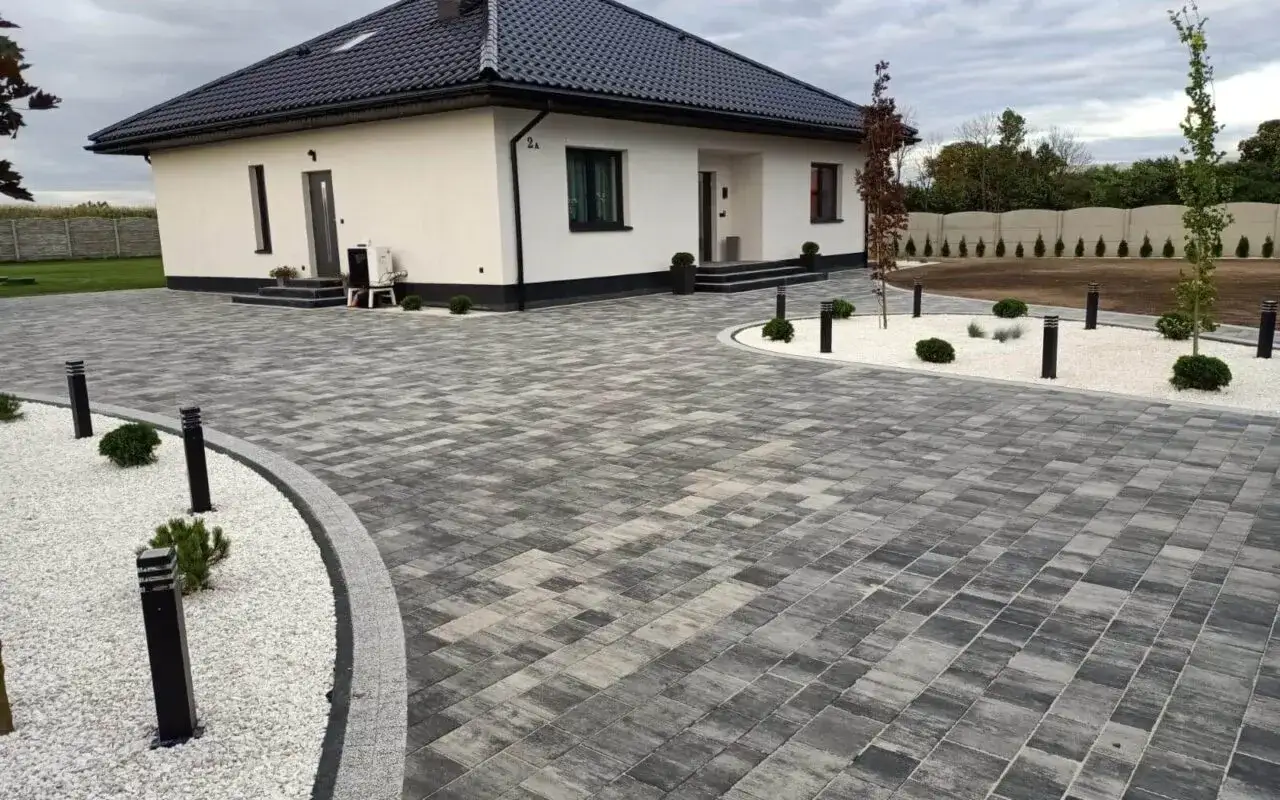 Nowoczesne podjazdy i ścieżki z różnych rodzajów kostki brukowej, tworzące elegancką mozaikę wokół białego domu.
