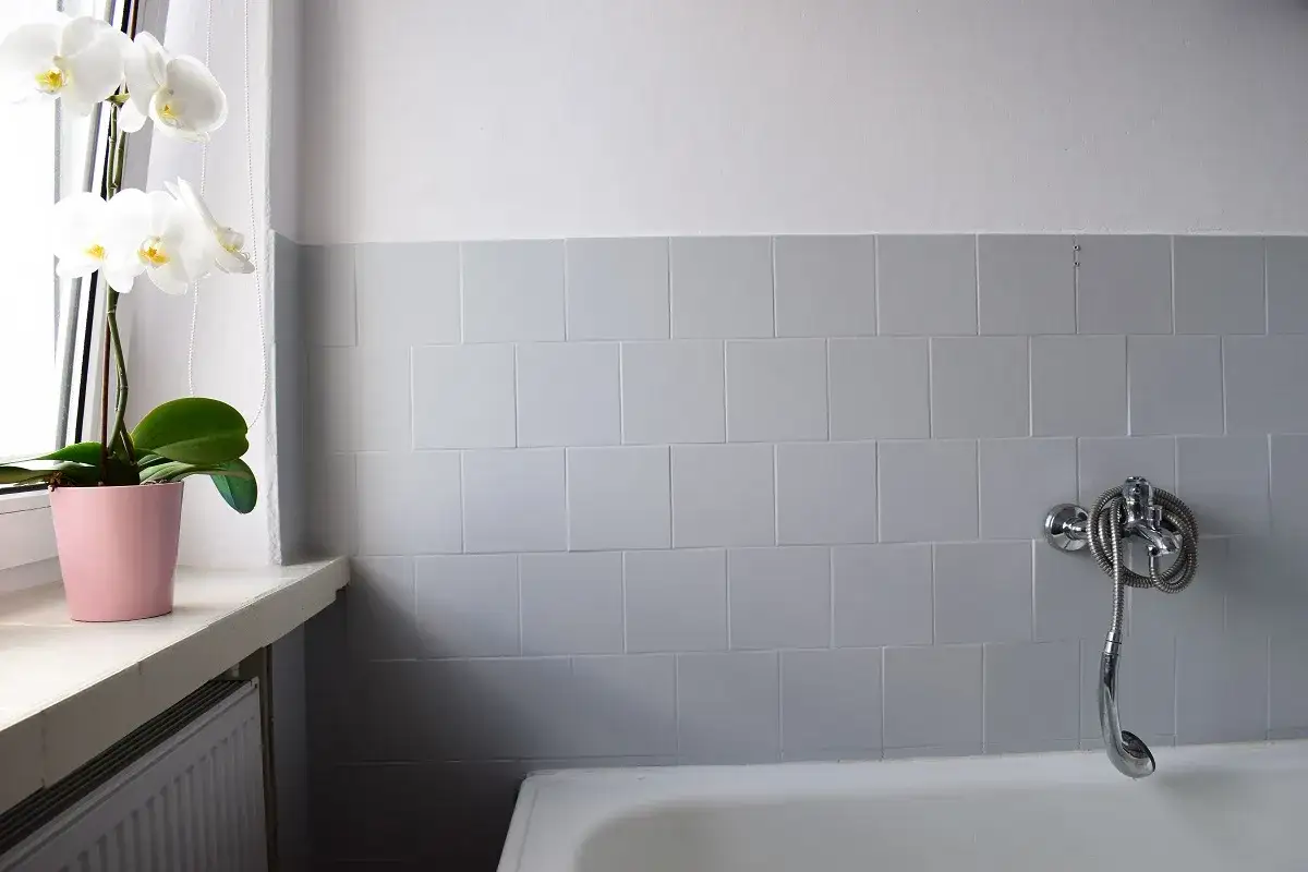 Łazienka po malowaniu płytek. Białe orchidee w różowej doniczce na parapecie. Prysznic nad wanną.