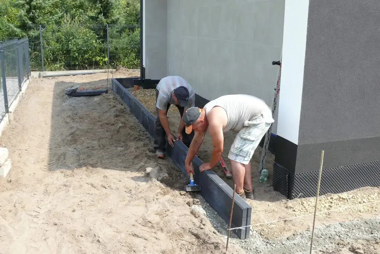 Dwóch mężczyzn układa obrzeża. Widać, że stosują odpowiednie suchy beton proporcje do stabilizacji.