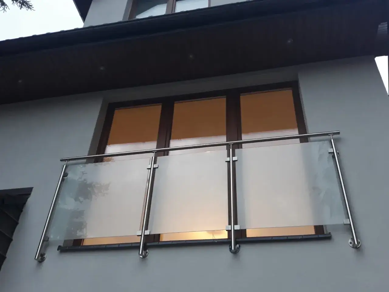 Nowoczesne balkony francuskie ze szklanymi panelami i stalowymi balustradami, zamontowane na szarej elewacji budynku.