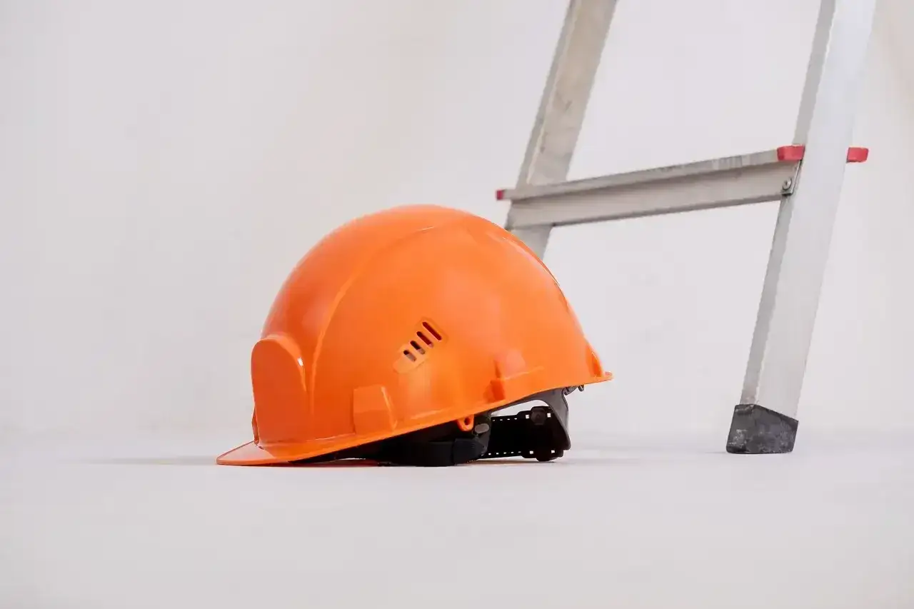 Pomarańczowy kask leży obok drabiny. To jeden z wielu kolorów kasków na budowie, symbolizujący bezpieczeństwo.
