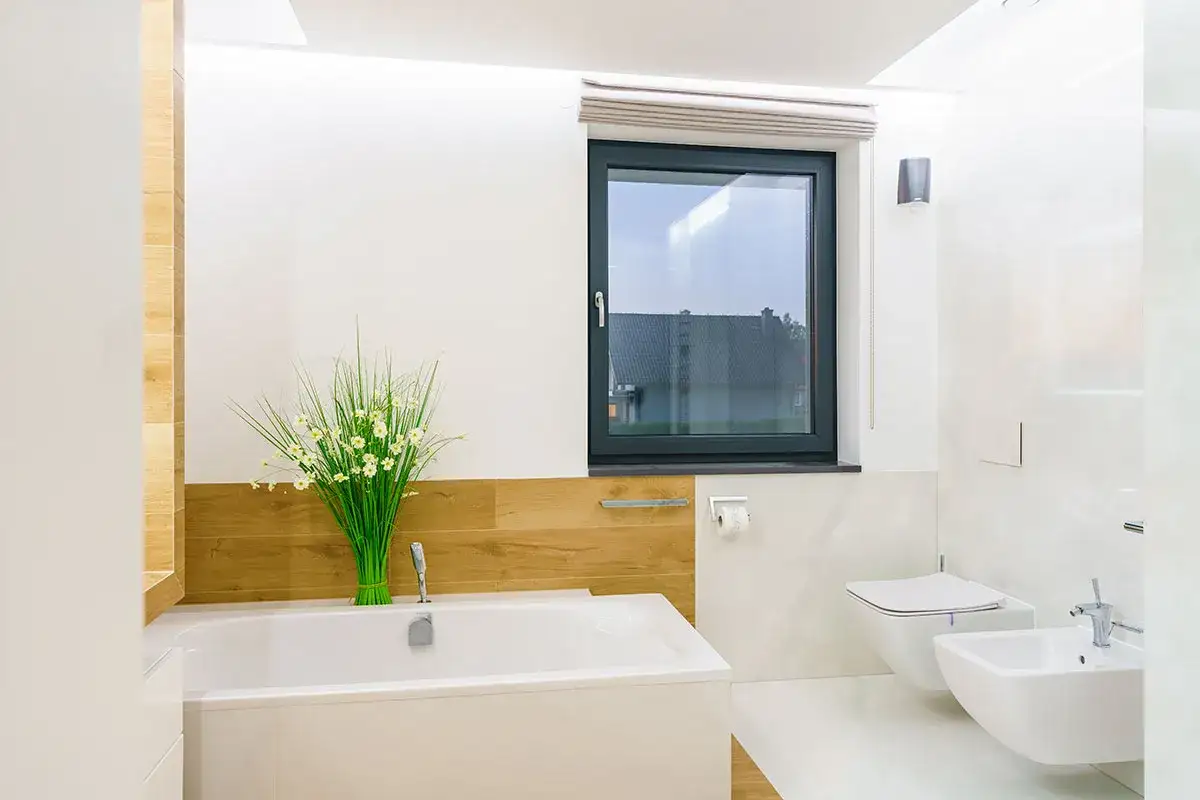Jasne, nowoczesne okno w łazience z widokiem na dom. Obok wanna i bidet.