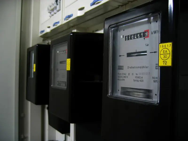 Rząd czarnych liczników energii elektrycznej. Na pierwszym liczniku widoczny odczyt 3104577 kWh.